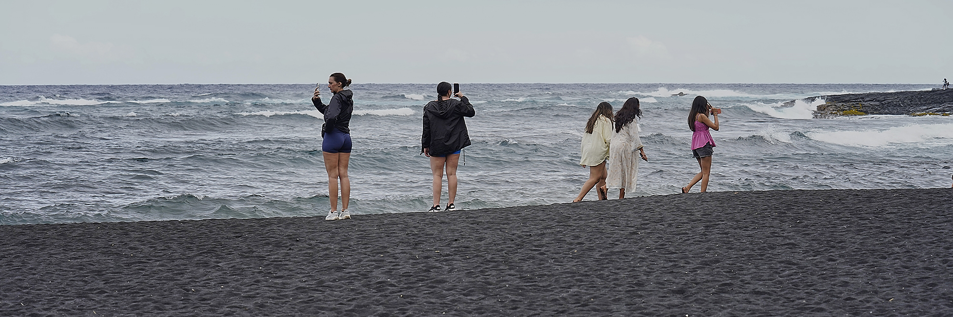 People walk and take pictures at Punaluʻu Black Sand Beach Friday, May 23, 2025, in Pāhala.